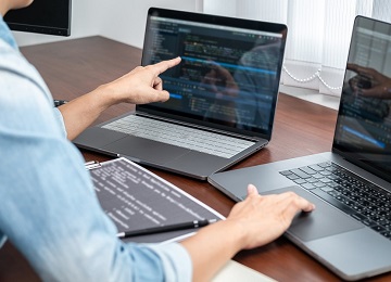 Asian programmer woman pointing and looking on multiple laptop screen to writing code and database while working about development website or applications in software development office